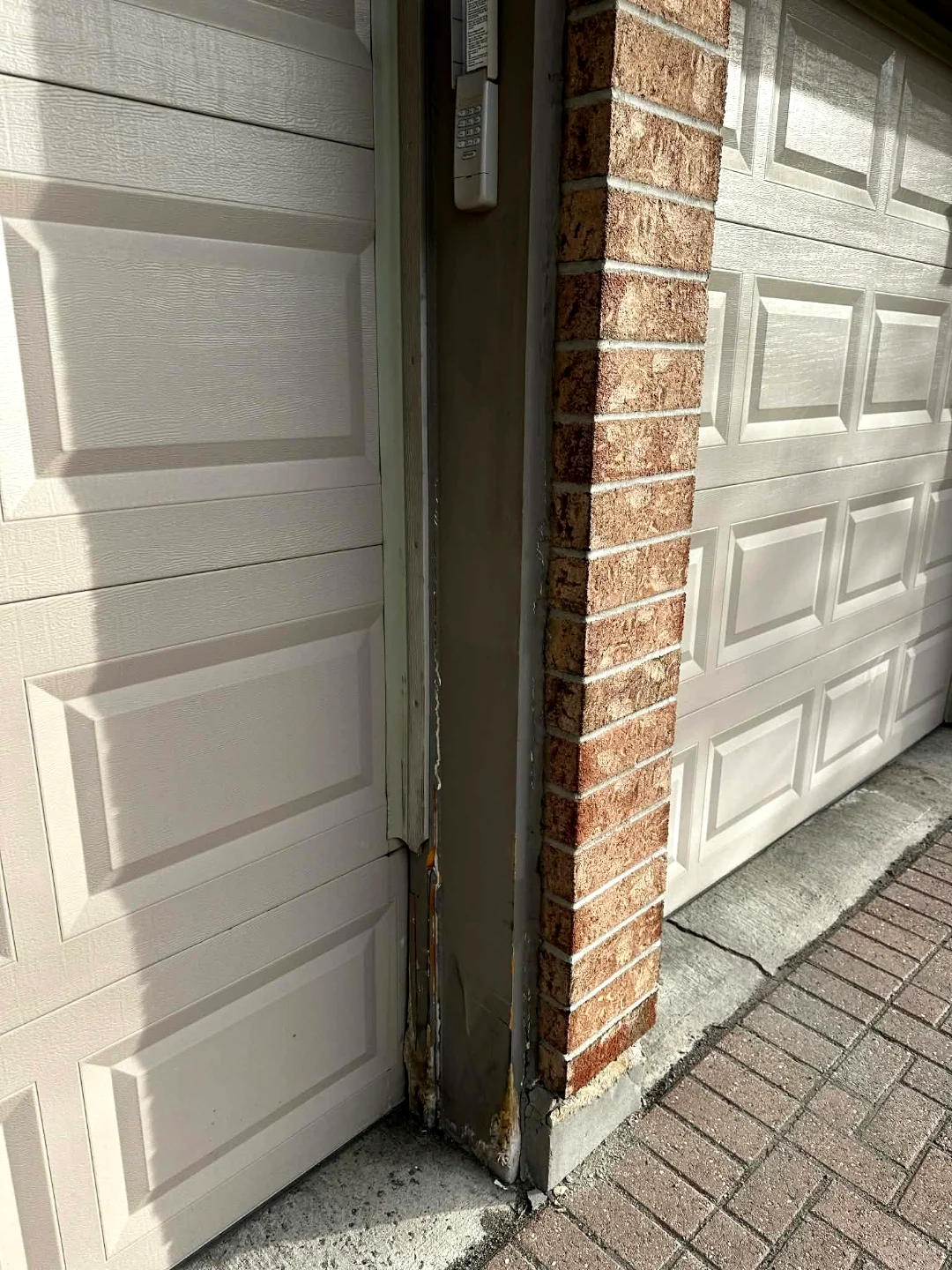 Before — Wood garage door trim peeling and rotting at the base between two cream raised-panel doors on a red brick Ottawa home