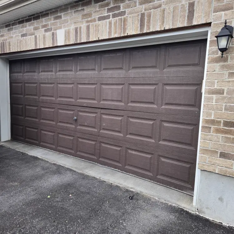 Before — Old dark brown raised-panel double-car garage door on a stone Ottawa home