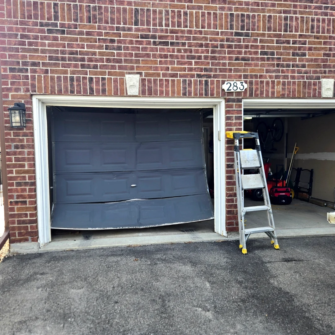 Before — Damaged charcoal garage door with the bottom panel buckled and out of the track on a red brick Ottawa townhome