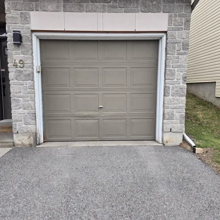 Before — Worn taupe raised-panel single-car garage door on a stone Ottawa home