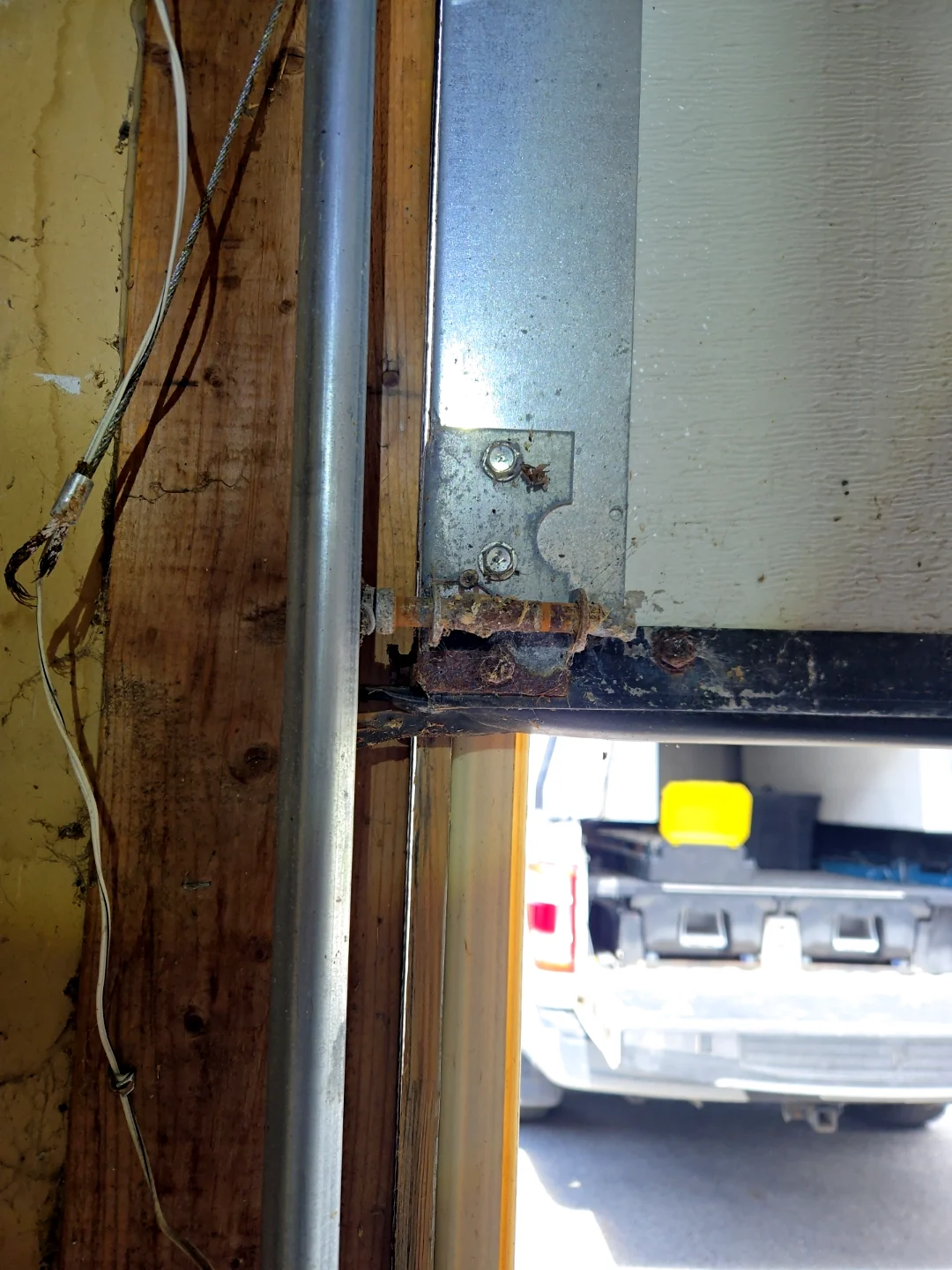 Close-up of a snapped, frayed garage door cable hanging beside a rusty bottom bracket on an Ottawa door before Liftime cable repair