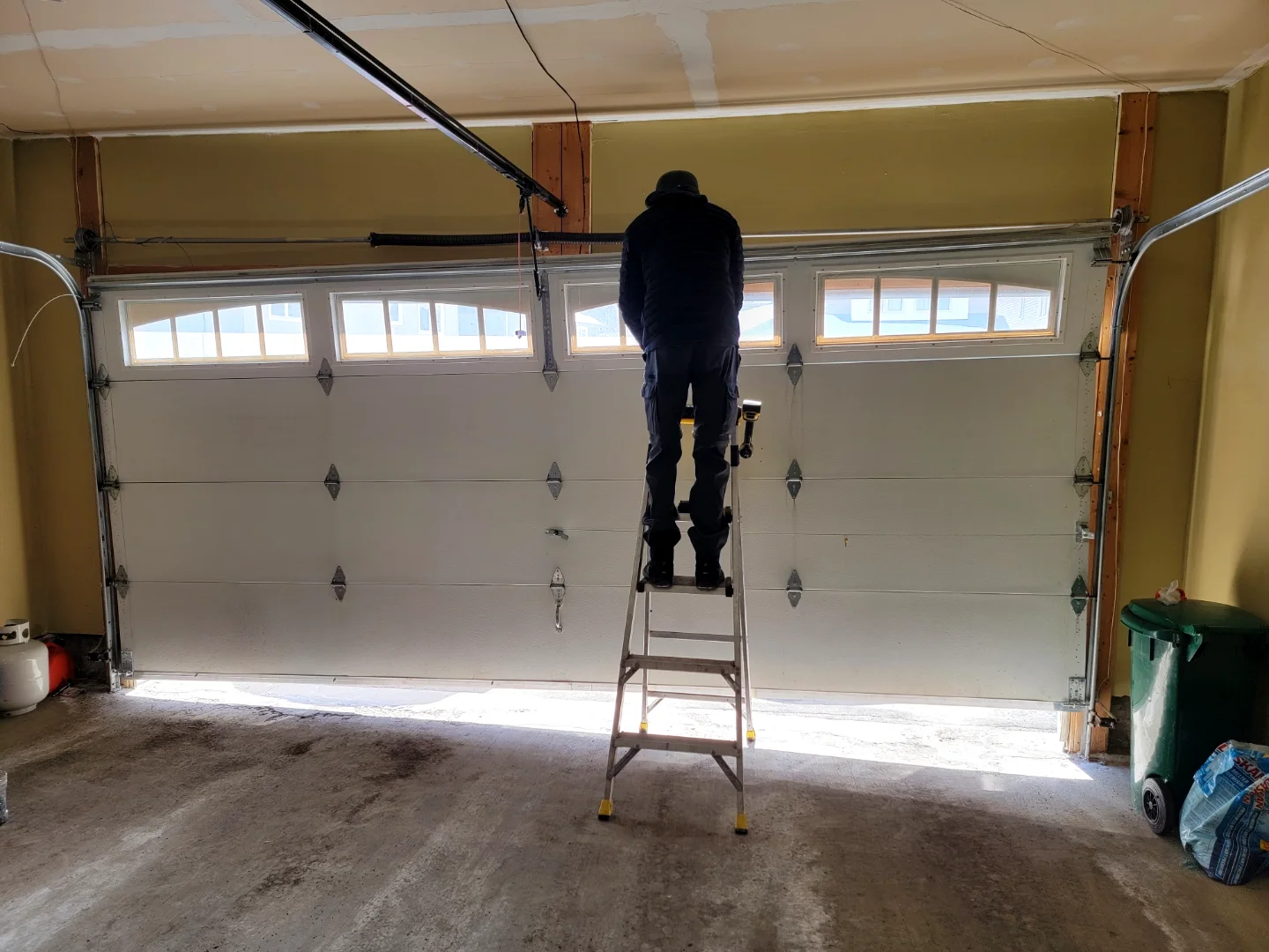 Liftime technician on a ladder working at the top of a garage door with the cables and opener visible in an Ottawa garage