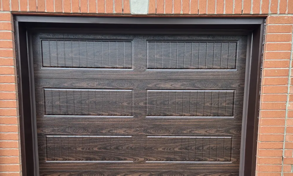 Dark brown aluminum capping around a woodgrain garage door in a brick opening
