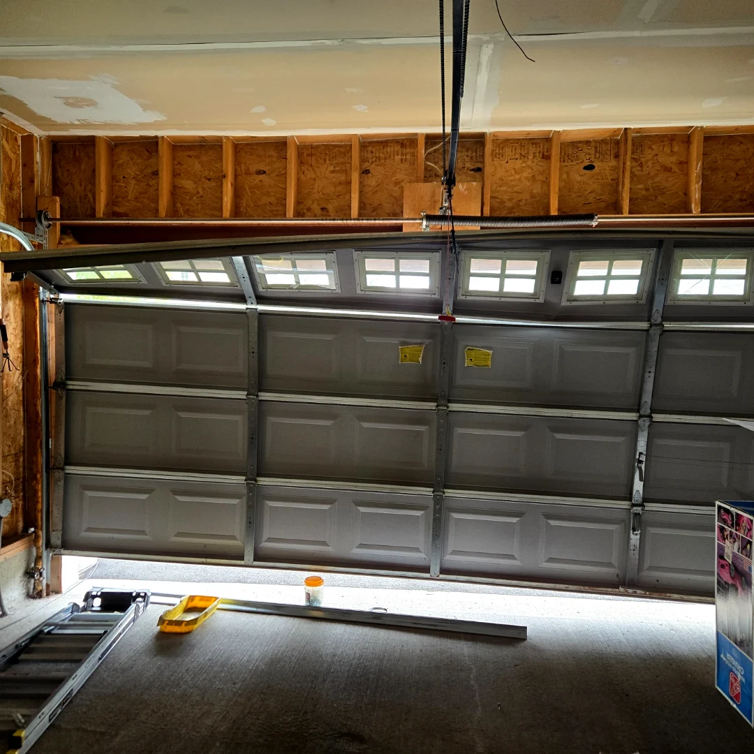 Garage door drooping at a sharp angle with a broken spring and panels pulling out of the track — an emergency call before Liftime repair