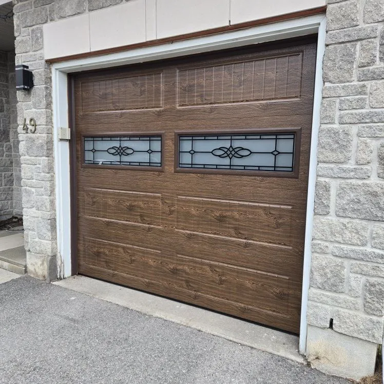 Single-car faux-wood brown carriage garage door with decorative glass on a stone Ottawa home