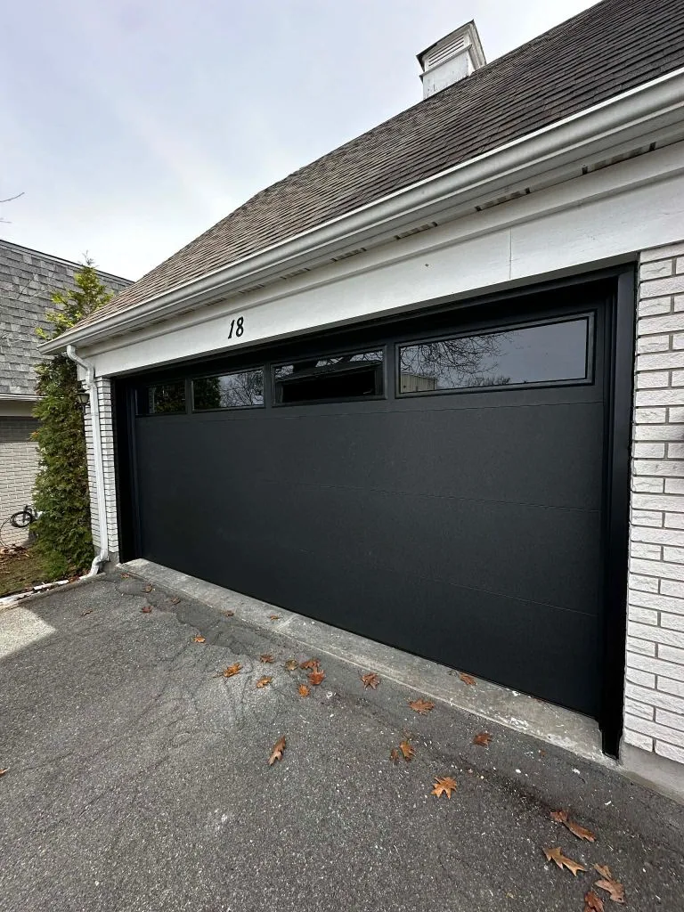Double-car black flush garage door with wide top windows on a white brick Ottawa home