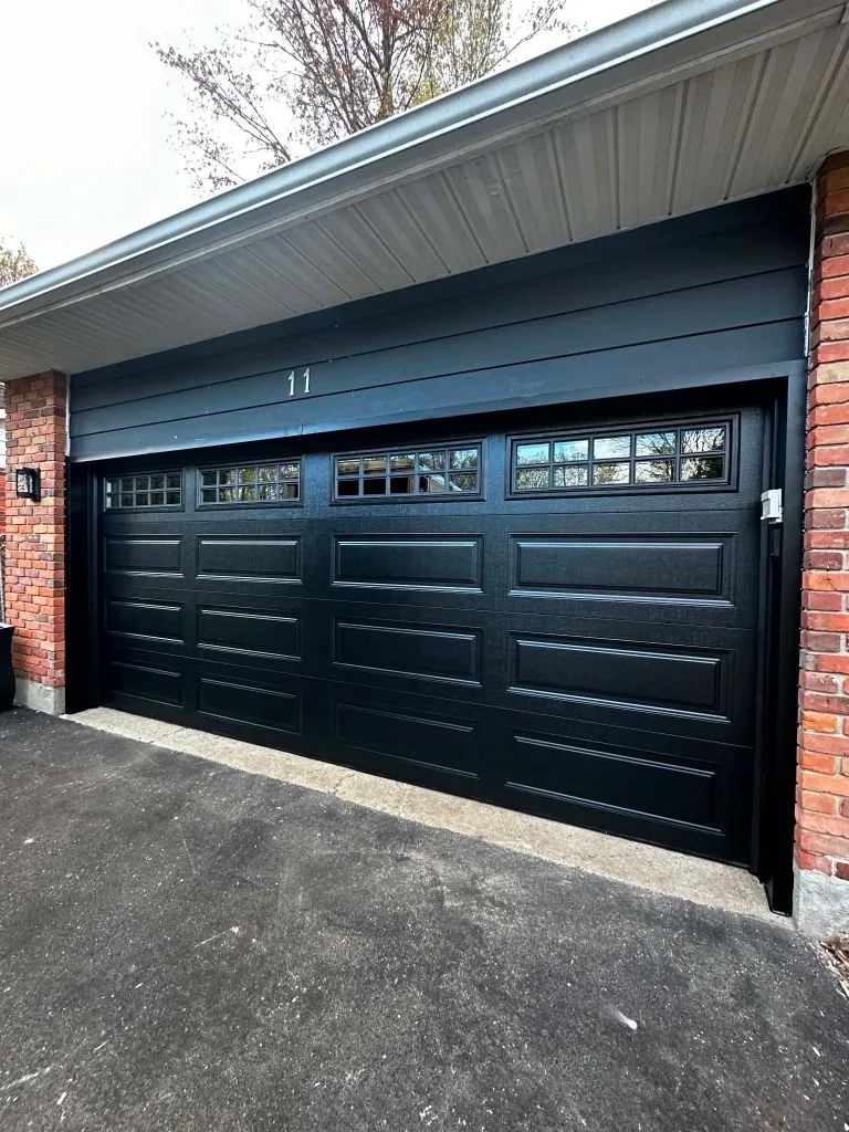 Double-car black raised-panel garage door with divided top windows on a brick Ottawa home