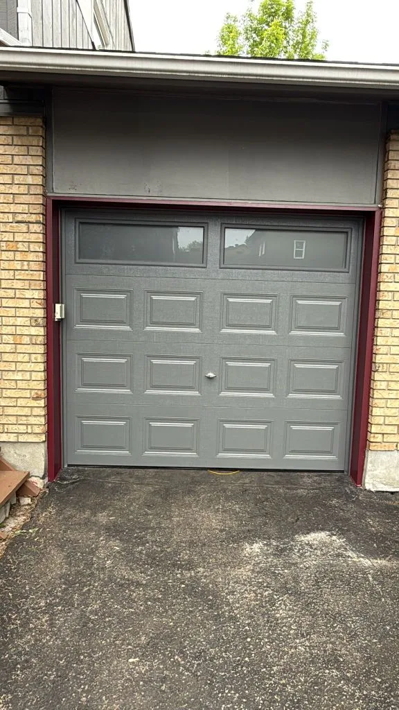 Single-car grey raised-panel garage door with top windows on a yellow brick Ottawa home