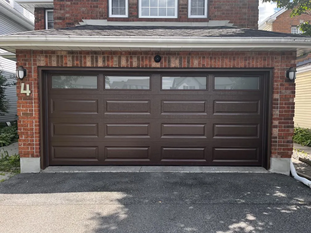 Double-car brown raised-panel garage door with top windows on a red brick Ottawa home