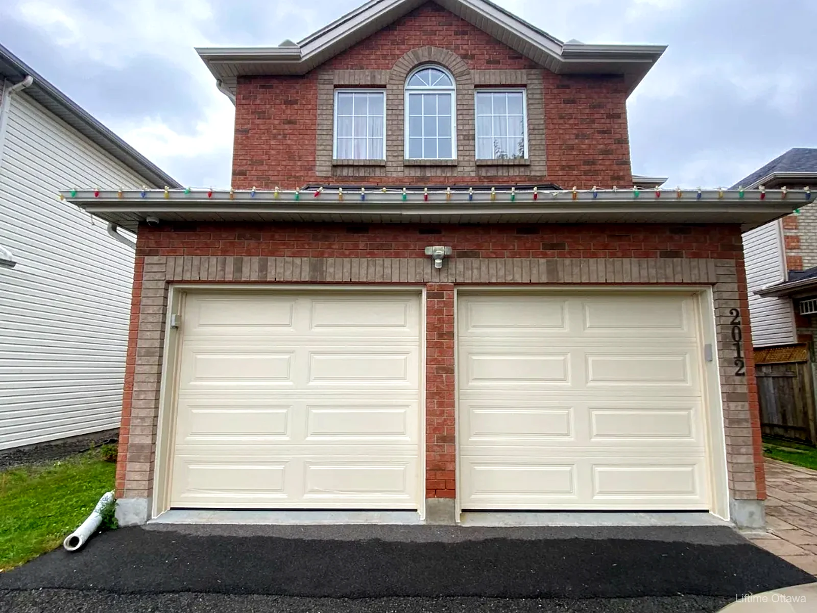 Pair of TOHO cream raised-panel garage doors on a brick Ottawa home, installed by Liftime
