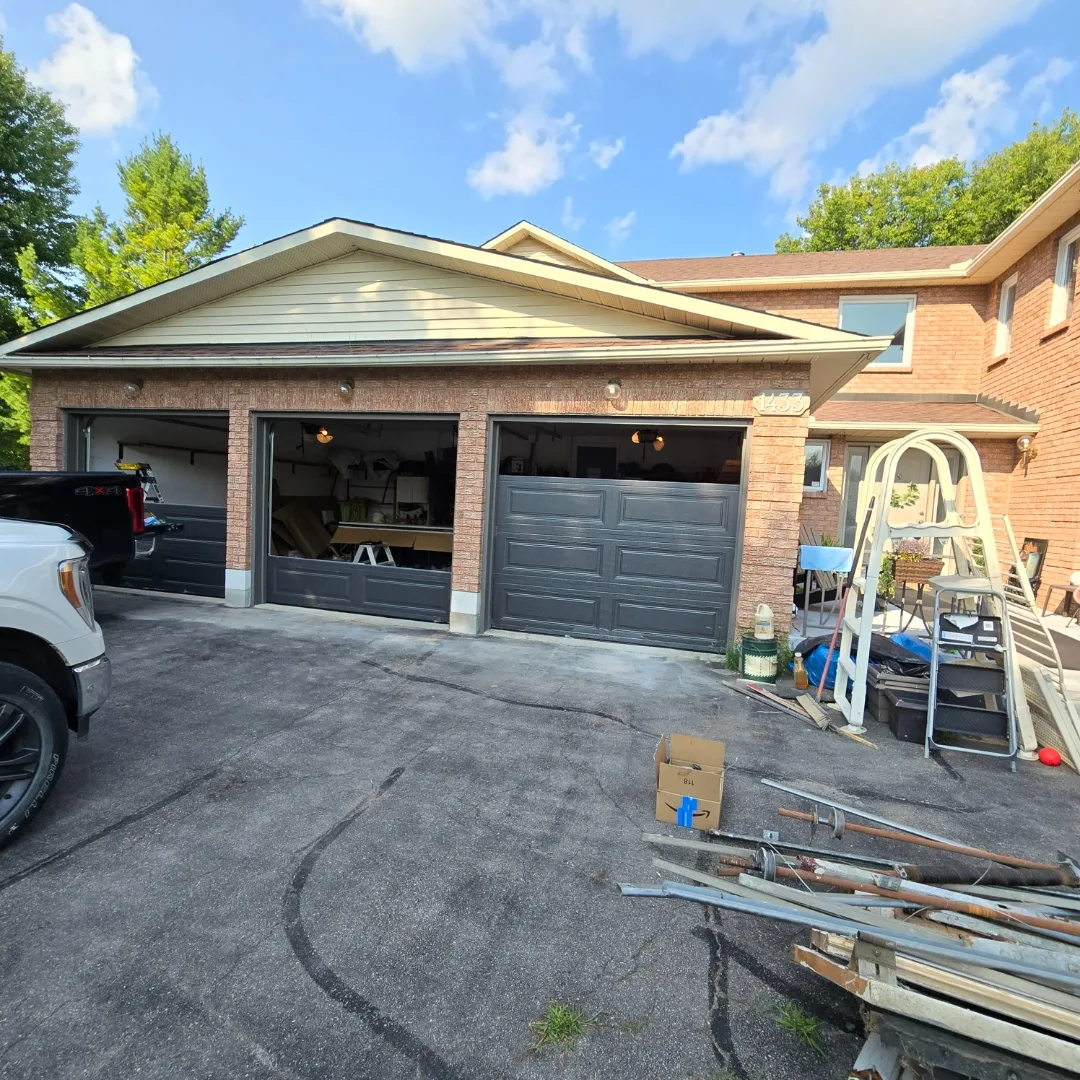 Mid-install photo of a triple-bay Ottawa garage with old doors removed and new black panels being prepped on the driveway by Liftime