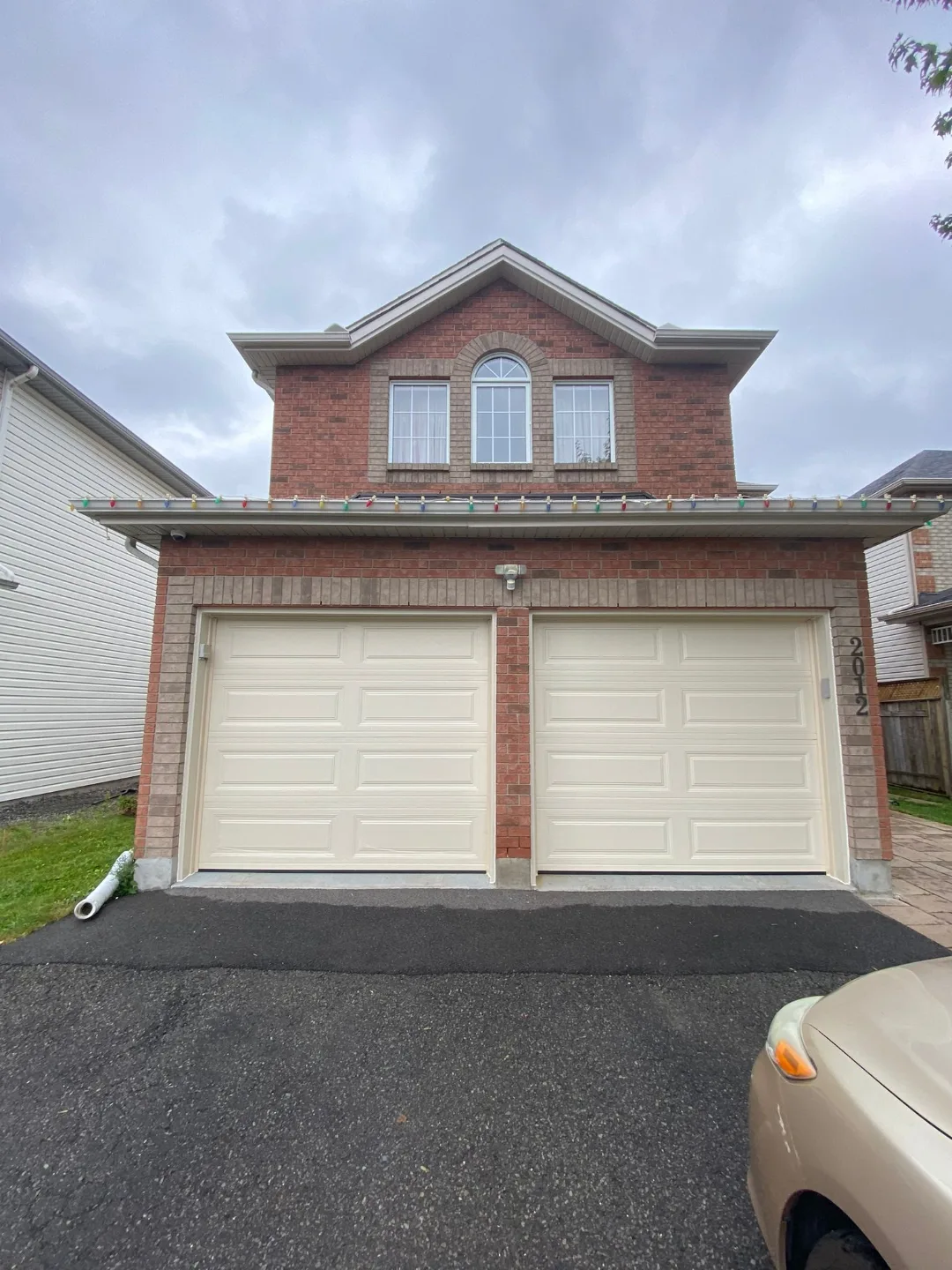 Pair of matching cream garage doors freshly installed by Liftime on a red brick Ottawa home with peaked dormer above