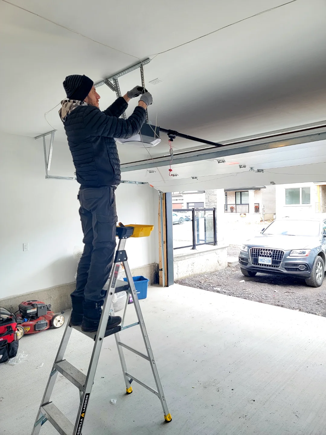 Liftime technician on a ladder wiring up a new ceiling-mounted garage door opener at a home in Ottawa