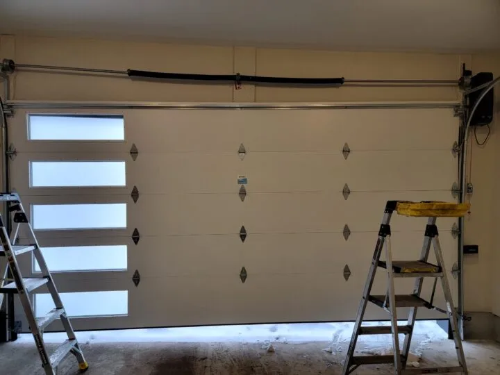 Interior view of a residential garage door showing the lift cables, drums, and torsion bar after a fresh install