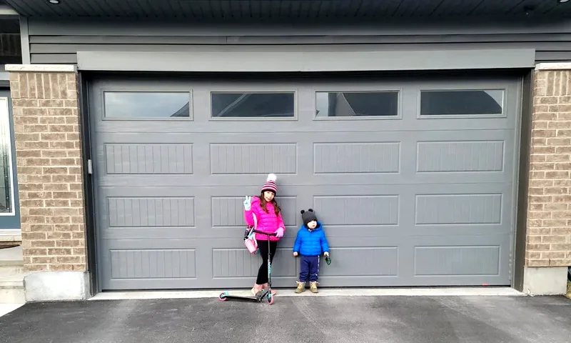 New grey insulated double garage door freshly installed by Liftime on an Ottawa home, with a young family standing in front