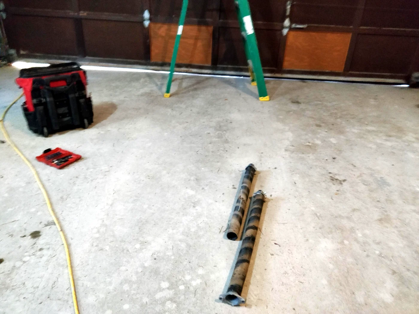 Two old broken torsion springs laid out on the garage floor next to a tool bag after Liftime removed them during a spring replacement in Ottawa
