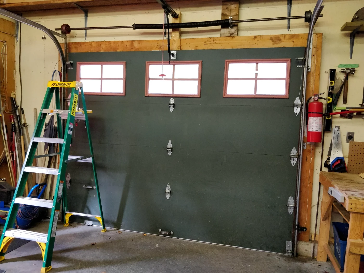 Hunter-green workshop garage door with a fresh new black torsion spring freshly installed across the top header by Liftime Ottawa