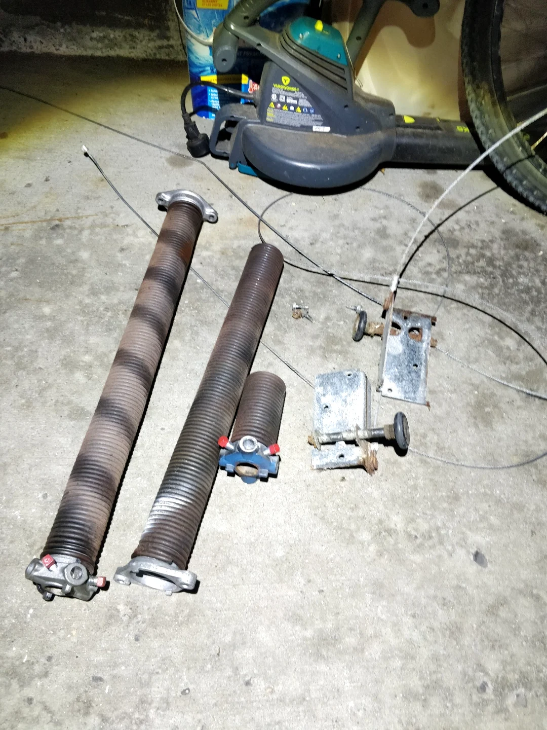 Old corroded torsion springs and worn cable removed from an Ottawa garage door, laid out on the floor next to the rusty mounting brackets by Liftime